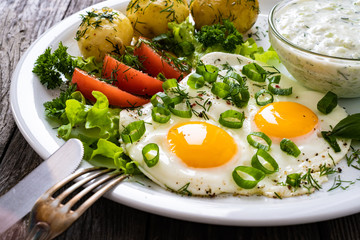 The best summer dinner - sunny side up eggs, boiled potatoes, cucumbers in yogurt  and fresh vegetables served on wooden table
