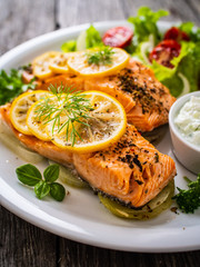 Roasted salmon steaks with lemon, cream sauce and vegetable salad served on wooden table
