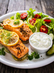 Roasted salmon steaks with lemon, cream sauce and vegetable salad served on wooden table

