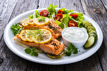 Roasted salmon steaks with lemon, cream sauce and vegetable salad served on wooden table
