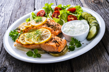 Roasted salmon steaks with lemon, cream sauce and vegetable salad served on wooden table
