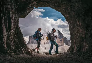 Gartenposter Dolomiten Couple of hikers walking, with Tre Cime di Levarado peaks on background, view from a cave window, in Dolomites, Italy. 