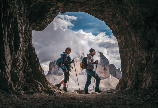 Couple of hikers walking, with Tre Cime di Levarado peaks on background, view from a cave window, in Dolomites, Italy. 