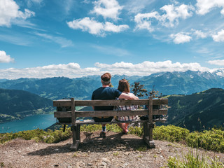Young couple sitting on bench on top of a mountain enjoying the scenery of Zell am Zee panorama in Austria - Powered by Adobe