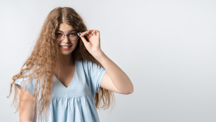 Portrait of modern girl in casual light clothes and wears round spectacles posing isolated on white wall background