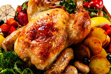 Roast chicken with vegetables served on cutting board on white background
