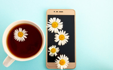 Tea with chamomile in a white Cup next to the phone and chamomile