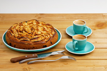 Homemade pie with apples and plums with almond petals and two cups of coffee espresso on wooden table.