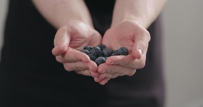 Slow motion man hands show big ripe blueberries on neutral background