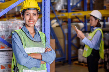 Warehouse woman wearing a hardhat standing cargo at goods or merchandise warehouse and check for control loading from Cargo freight ship for import and export by report on tablet. Teamwork concept