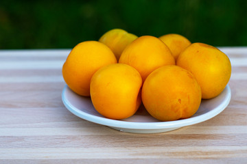 The yellow plum lies on a white plate on a wooden light table