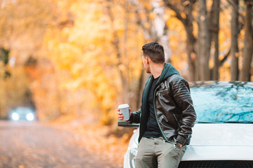 Young man drinking coffee with phone in autumn park outdoors