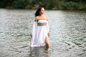 Young european woman with brown hair dressed a long white wedding dress stays in the river
