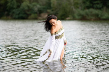 Young european woman with brown hair dressed a long white wedding dress stays in the river