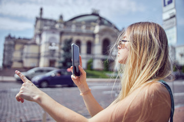 Cheerful pretty girl with long hair in sunglasses holding black smartphone outdoors close up