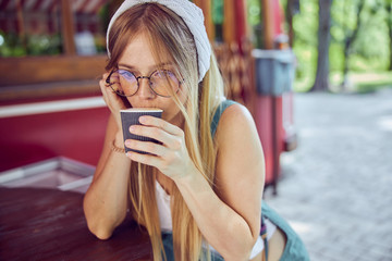 Fototapeta premium Pretty red-haired girl in glasses drinking coffee in cafe