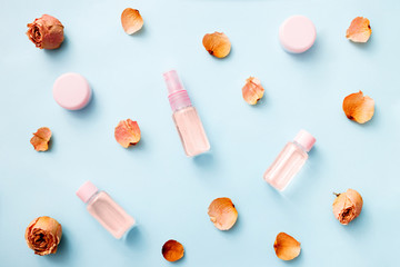 Flat lay of flowers and cosmetics products with Rose essential oil: toner, serum, essence, moisturizer and others on blue background, top view, banner. Facial Skin care beauty.