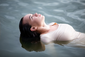 Young European woman with dark hair in wet closes posing in water 