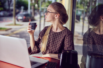 Red-haired girl with freckes in glasses is going to work on laptop a side view