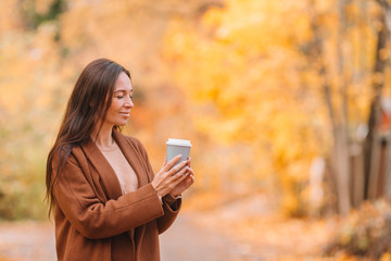 Fall concept - beautiful woman drinking coffee in autumn park under fall foliage