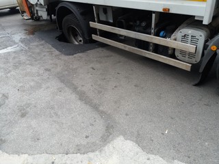 Manto stradale collassato sotto il peso di un camion, con la ruota incastrata nella buca