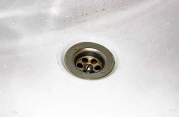 Drain in the center of the white unwashed sink.