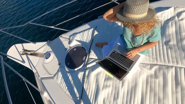 Adult modern woman use laptop computer technology to search the web and smart work on a boat deck in a nice weather sunny day - online people generation concept