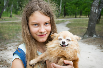 In summer, in the forest, a girl holds a dog in her arms. They are smiling.