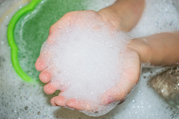 Fototapeta premium above the water with a bucket in the bathroom in children's hands soap foam