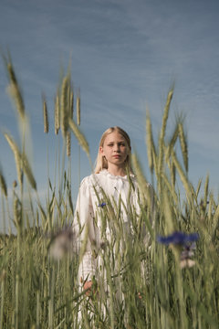 Young blonde girl in white dress in field of wheat under a blue sky