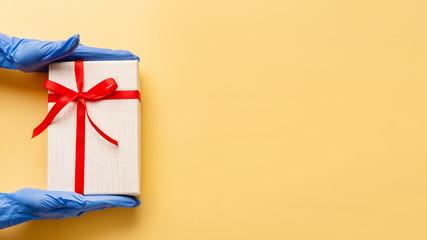 Birthday surprise. Pandemic hygiene. Hands in protective gloves holding present box red ribbon....