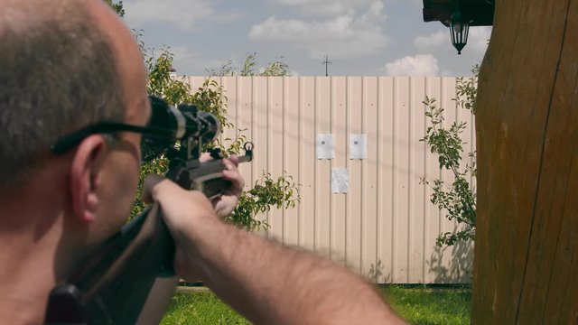 Close up of the face of a man aiming at an impromptu paper target while looking into an optical rifle sight.