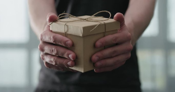 Slow motion young man shows brown craft paper gift box