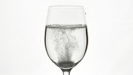 pill of effervescent aspirin in elegant glass with water, white background