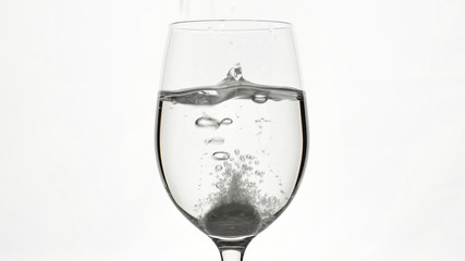 pill of effervescent aspirin in elegant glass with water, white background