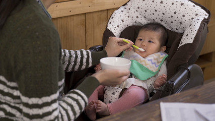 lovely asian toddler eating meal given by her mummy in a stroller. portrait of adorable baby trying...