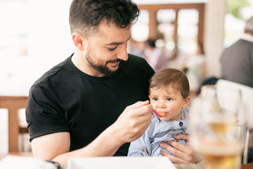Bearded father feeding little baby son in restaurant