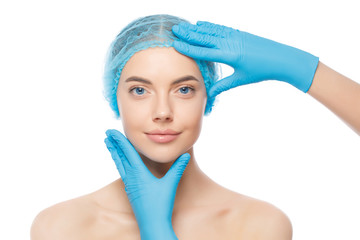 Young beautiful woman wearing medical cap examined by doctor of beauty clinic in gloves before treatment, isolated on white background