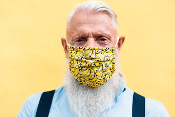 Hipster senior man wearing trendy face mask during coronavirus outbreak - Old fashion and washable eco cotton concept - Focus on mask