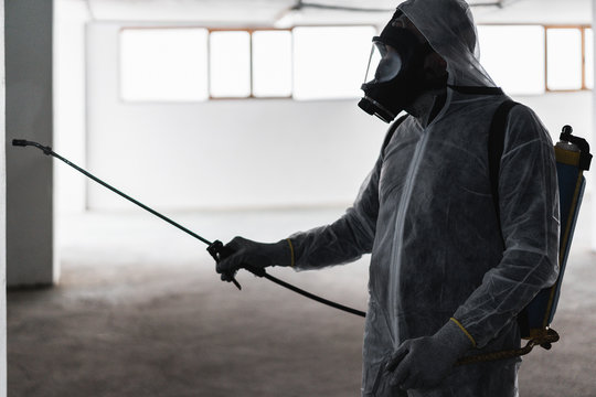 Worker in hazmat suit making disinfection inside city park building - Coronavirus decontamination for people healthcare - Focus on face black mask