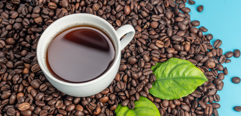 White cup with freshly brewed aromatic coffee and coffee beans on a blue background