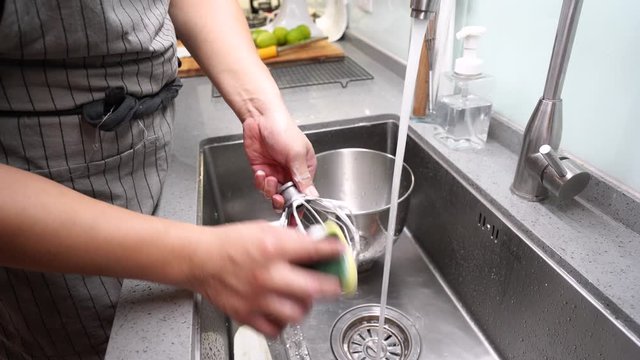 Anonymous person washing wire whisk in sink