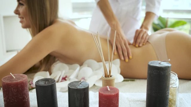 Back massage on massage table with flowers and candles to beautiful blonde girl in modern spa center. Rehabilitation and health. Relax