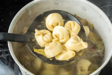 Ordinary handmade meat dumplings with bay leaves on ladle above the saucepan.
