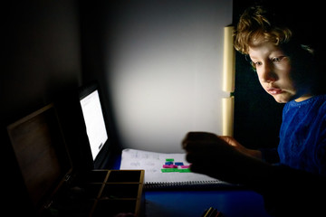 Fototapeta na wymiar Boy studying mathematics at night alone in his dark room with Montessori material.