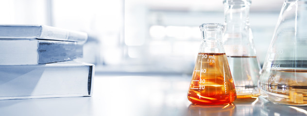 glass flask with orange solution and text book in chemistry laboratory school education banner...