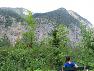 Fototapeta na wymiar Woman sitting on bank enjoying view in front of mountain range and forest