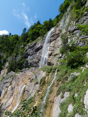 Rock face with waterfall streaming down in the middle, blue sky in background and greenery on sides