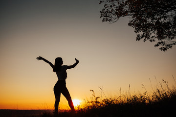 Fototapeta premium The silhouette of the girl on a background sunset. Happy girl in a field take selfie on a smartphone. Copy space.