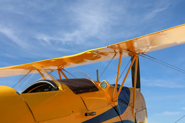 Classic biplane trainer aircraft. Yellow against blue sky.